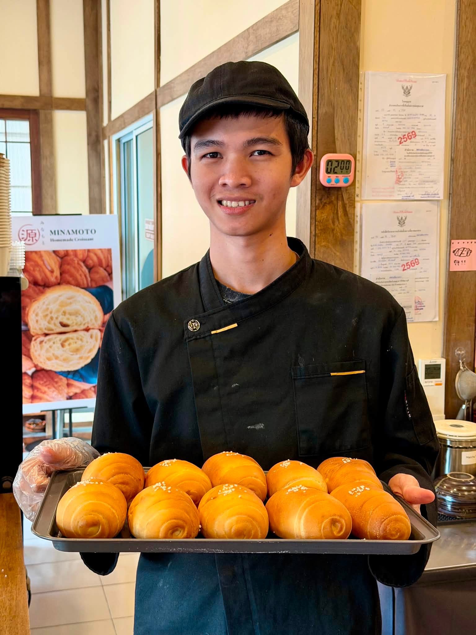 พนักงานร้าน Minamoto ยิ้มถือถาดขนมปังที่เพิ่งอบเสร็จใหม่ๆ